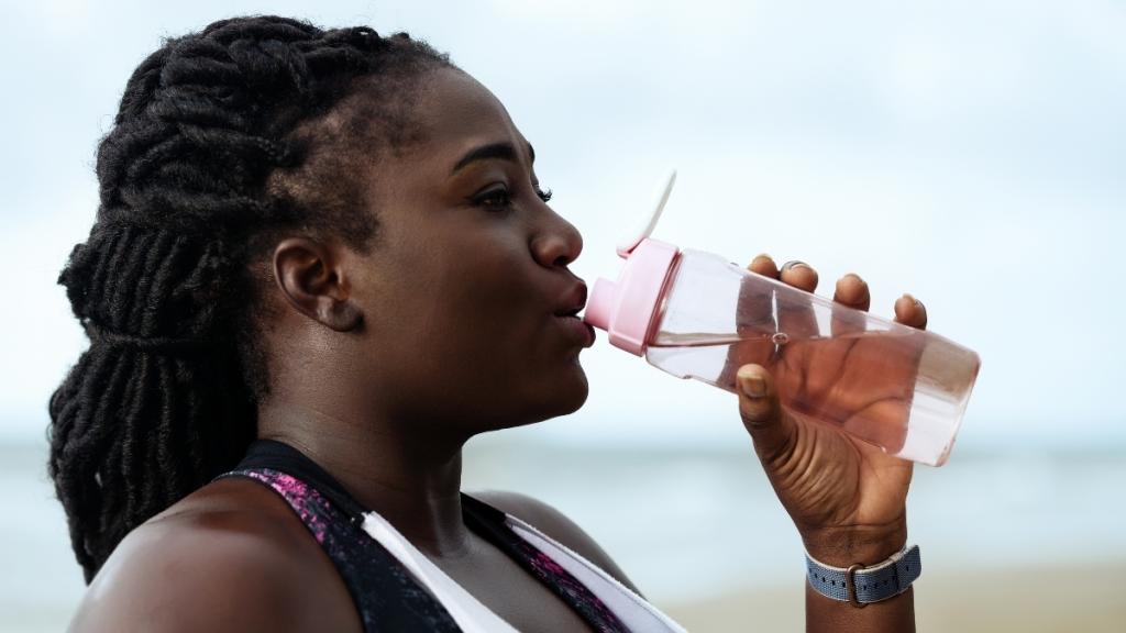 Woman in workout clothes drinks from a water bottle.