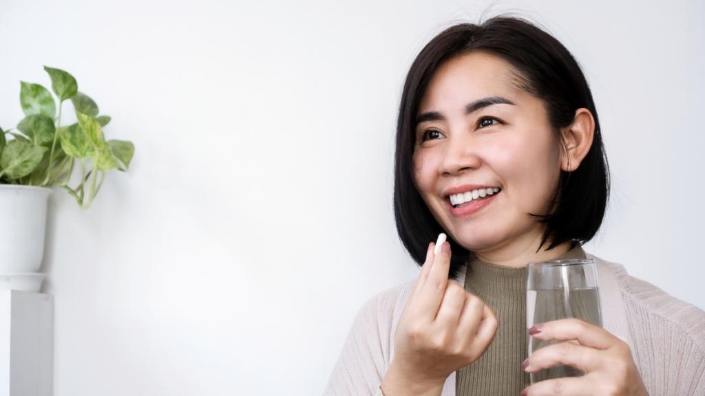 Woman taking a pill while holding a glass of water.