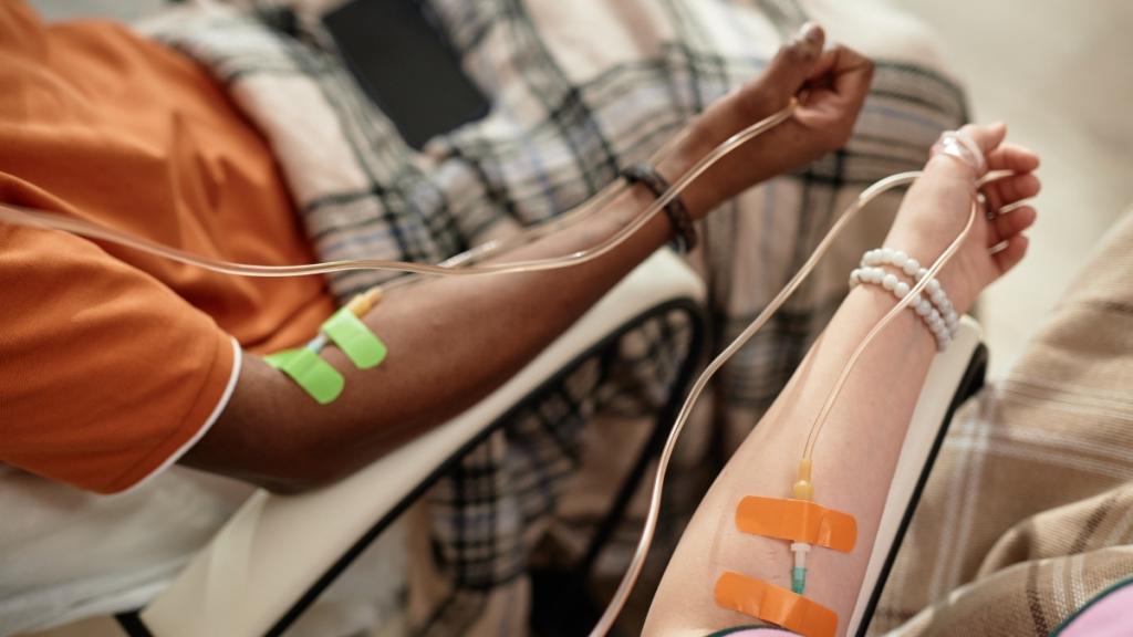 Two people get IV infusions with their arms next to each other.
