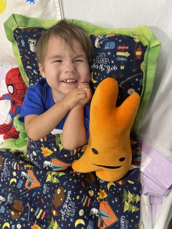 Young boy in hospital bed with stuffed animals smiles