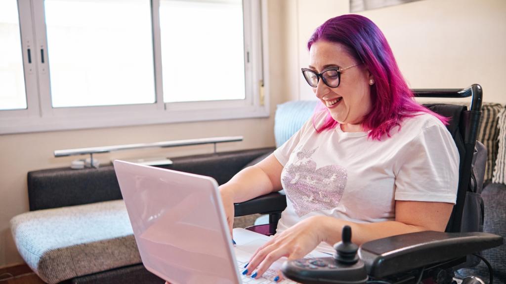 Lady with colorful hair on computer in motorized wheelchair.