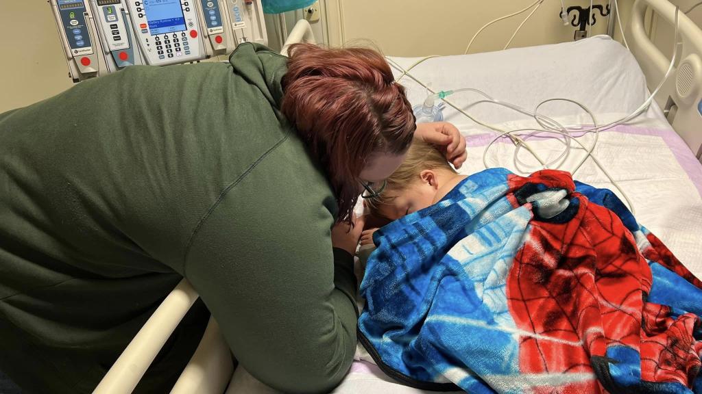 Mother hugs her young son lying in hospital bed