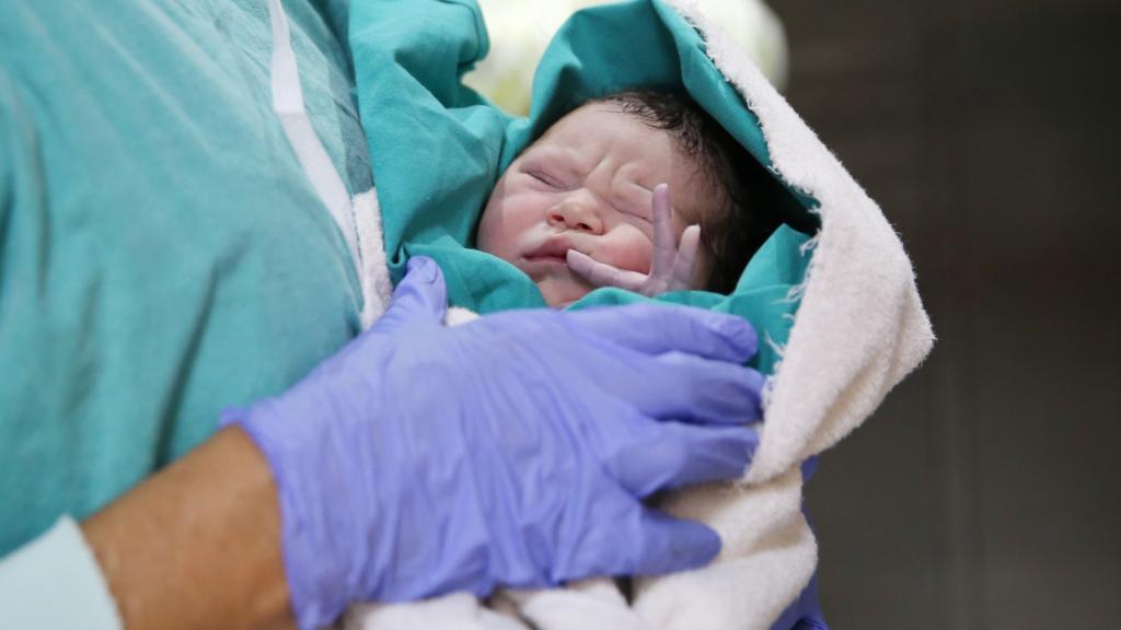 Newborn baby held by healthcare provider.
