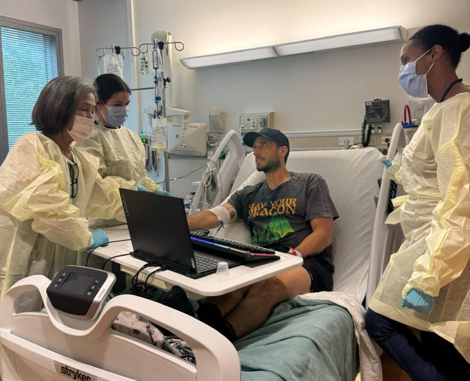 Chris Simpson in hospital bed surrounded by health team