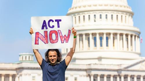 Man holding "Act now" sign in front of the U.S. Capitol building.