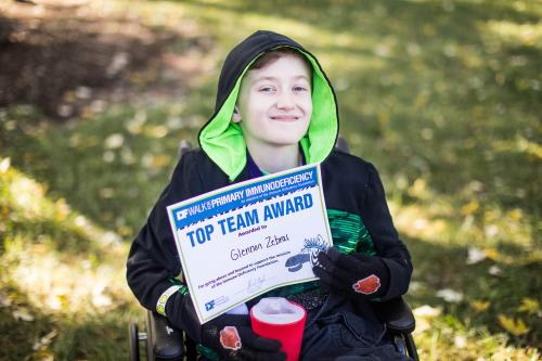 Kid in wheelchair holds "Top Team Award" certificate at St. Louis 2019 Walk for PI.