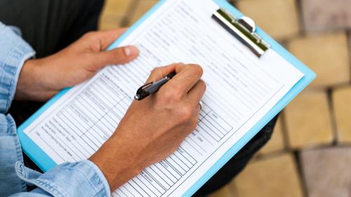 Person using pen and clipboard to fill out paperwork.