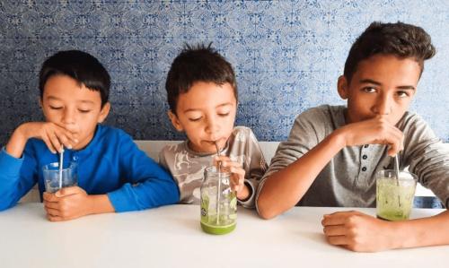 Three boys drinking green juice at a table.