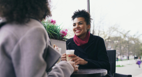 Person holding a coffee cup while talking with another person. 